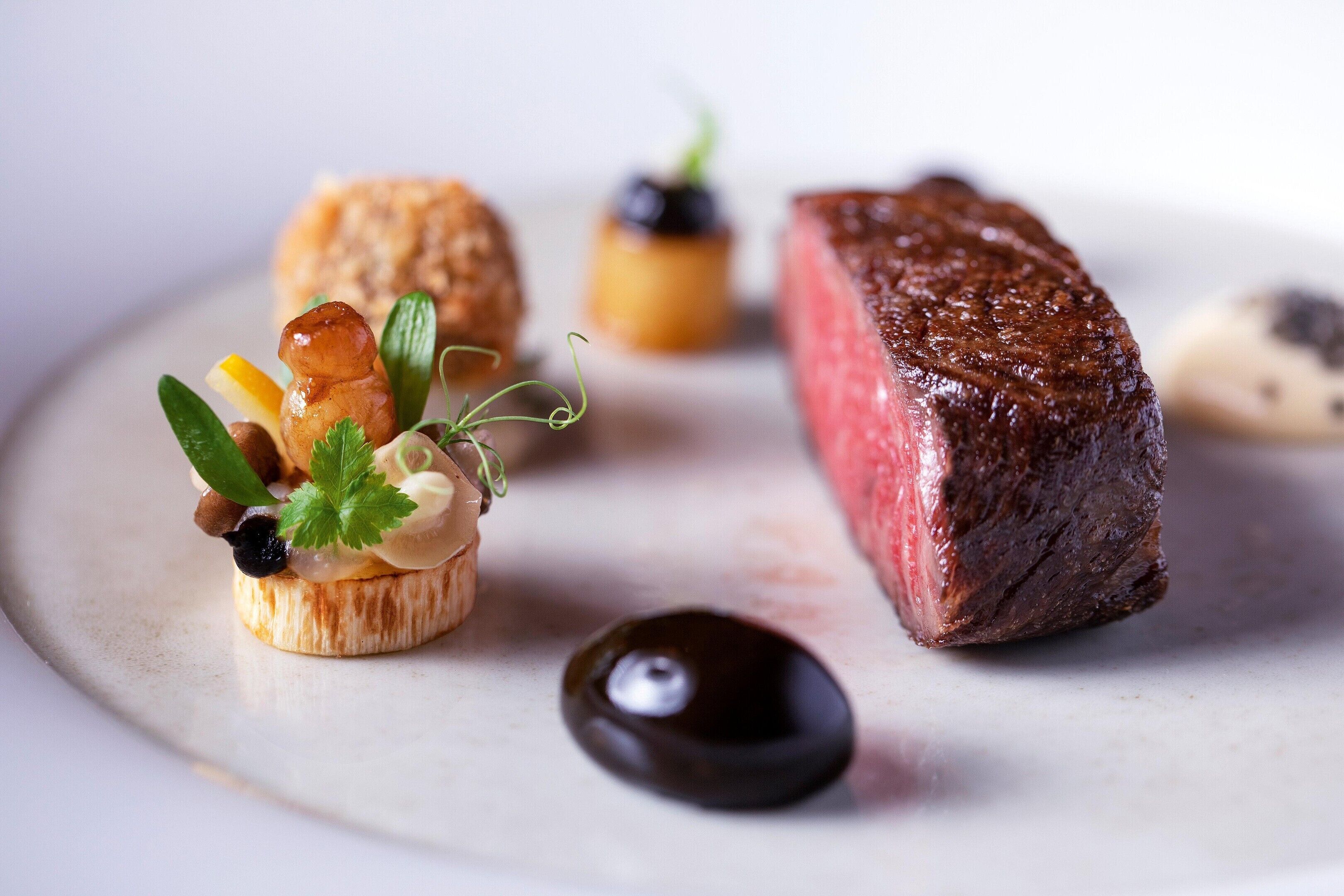 A steak with a side of vegetables and a small dish of sauce.