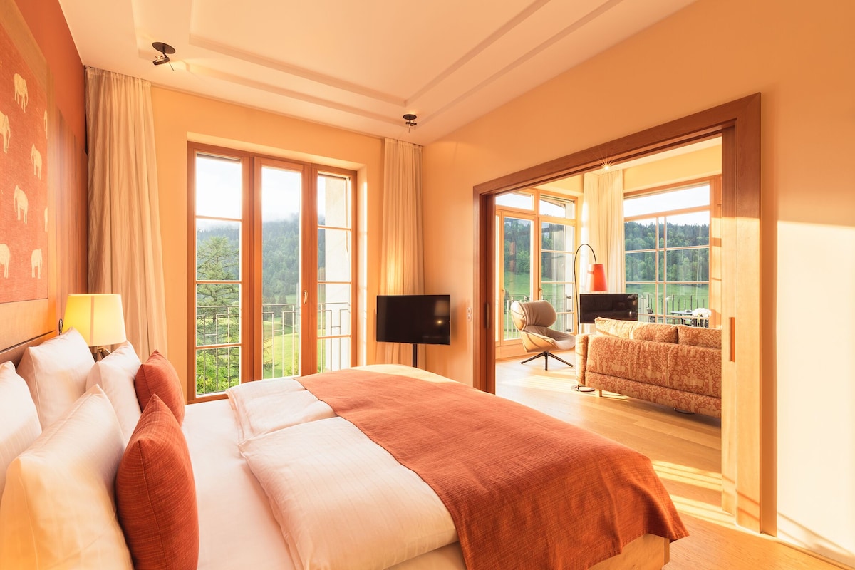 A spacious bedroom with a large bed, a television, and a balcony with a view of the outdoors.