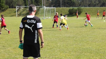 Players engage in a lively soccer match on the field surrounded by a fence and trees.
