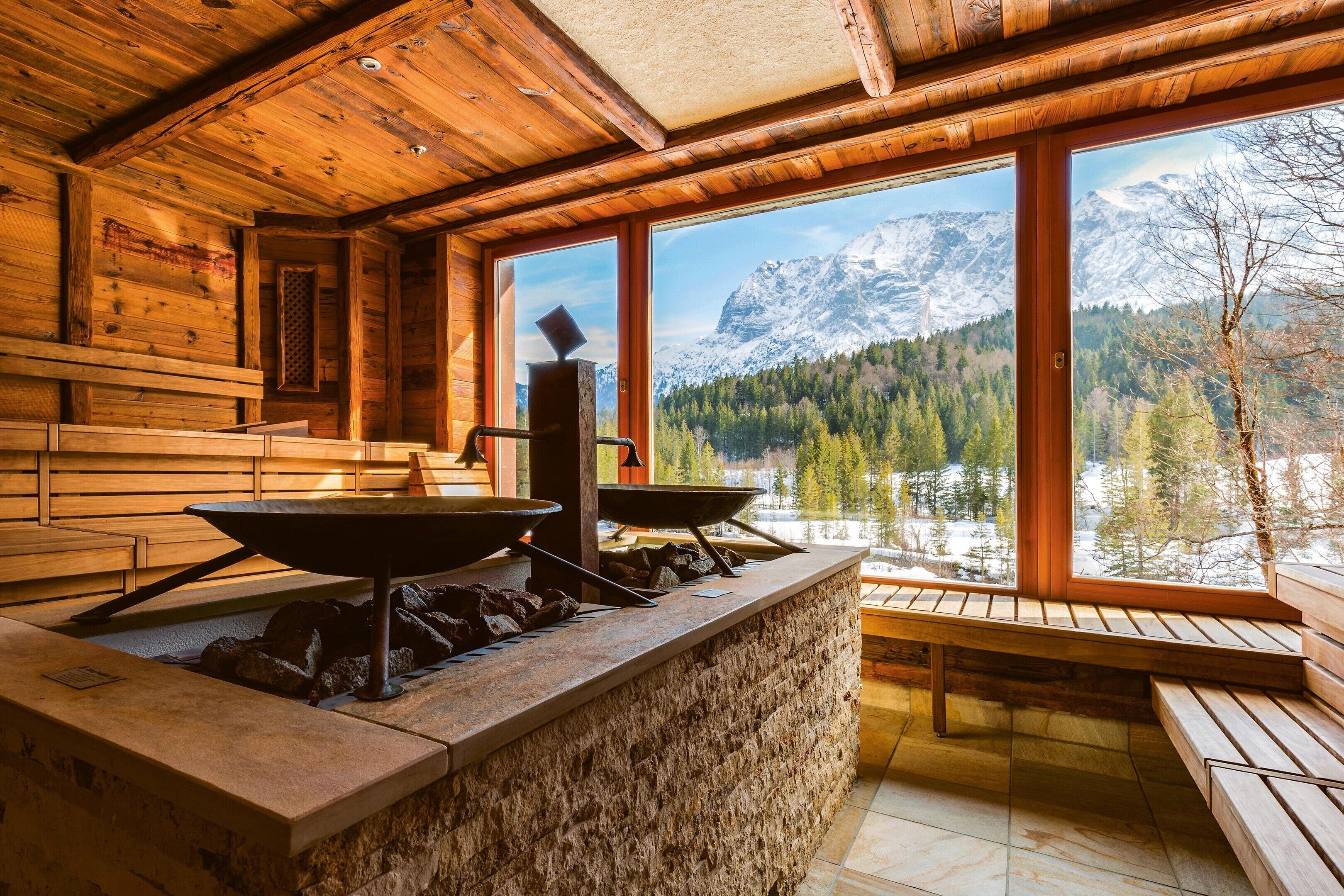 Ein rustikales Blockhaus-Interieur mit einer Steintheke, Holzbanken und Blick auf schneebedeckte Berge.