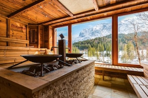 A rustic cabin interior with a stone counter, wooden benches, and a view of snow-capped mountains. - Schloss Elmau Luxury Spa Retreat & Cultural Hideaway (Kruen)