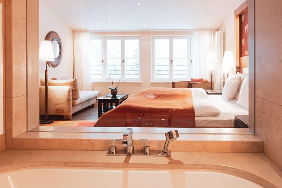A modern bedroom with a large bed, a sitting area, and a bathtub.