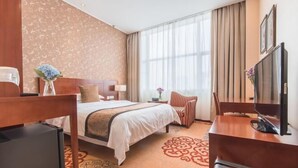 Une chambre d’hôtel comprenant un lit, un bureau avec une télévision, une chaise, une table de chevet et une fenêtre avec des rideaux.