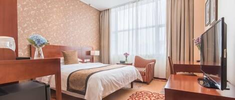 Habitación de hotel con cama, escritorio con televisor, silla, mesita de noche y ventana con cortinas.