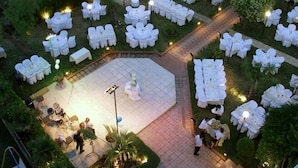 Amplio espacio exterior para eventos, con mesas y sillas circulares, rodeado de follaje y senderos.