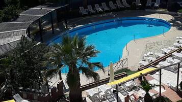 Una piscina con sillas de descanso y sombrillas, rodeada de palmeras y un área techada.