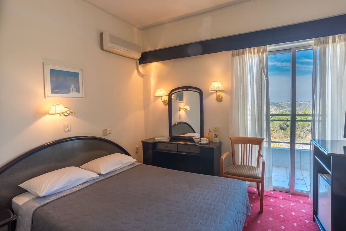 A hotel room with a bed, a dresser, a mirror, a chair, and a balcony with a view.
