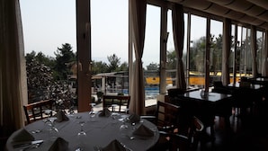 Un restaurante con mesas redondas dispuestas para comer, con amplias ventanas que ofrecen vista a una piscina y follaje.