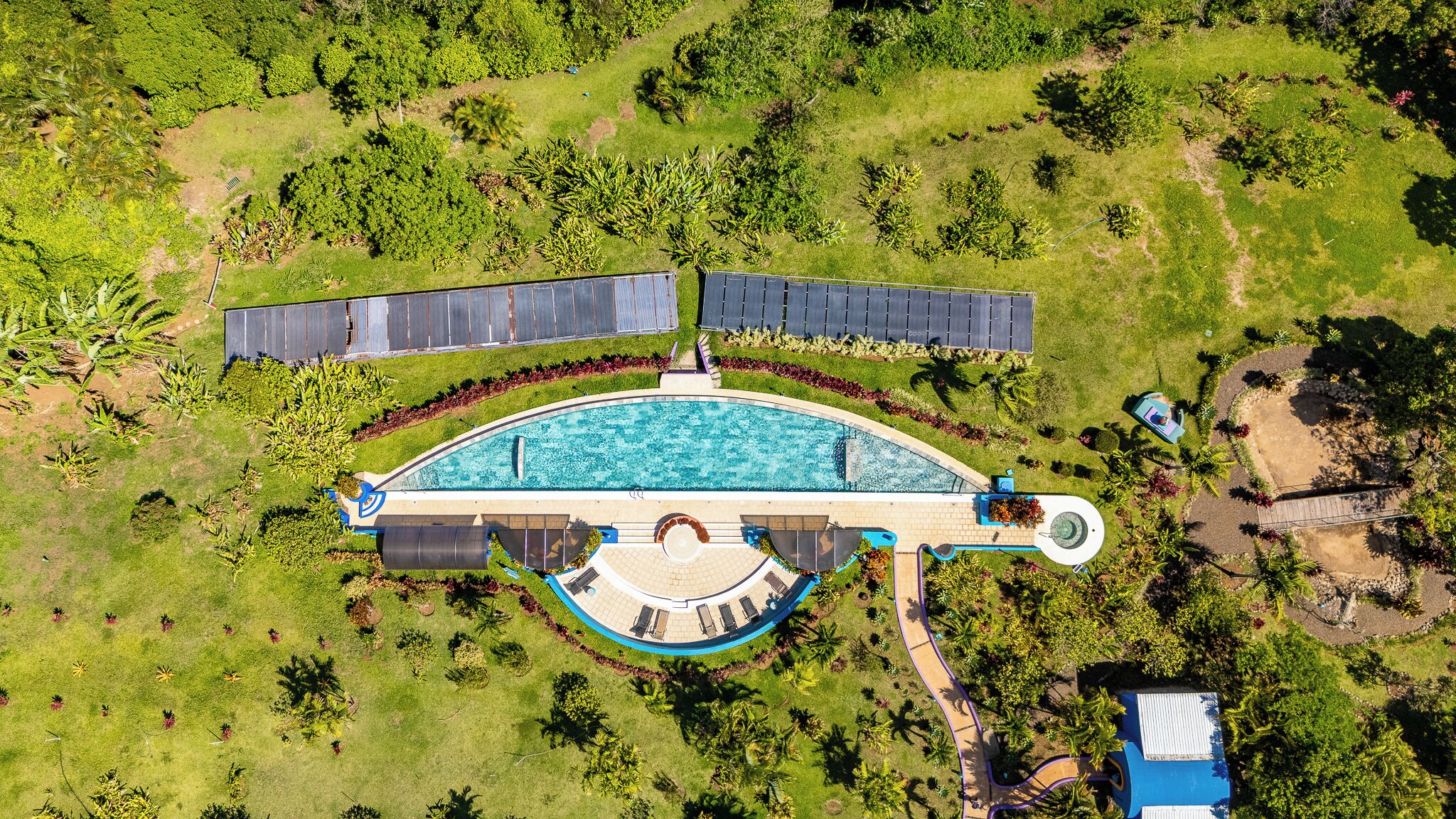 An aerial view of a resort with a large swimming pool, solar panels, and lush landscaping.