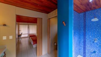 A hotel room with a wooden ceiling, a bathroom with blue mosaic tiles, and a bed with red bedding.