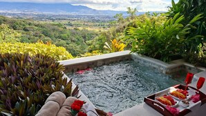 A hot tub with a view of a city and mountains, surrounded by lush greenery. - Xandari Resort And Spa (San Isidro)