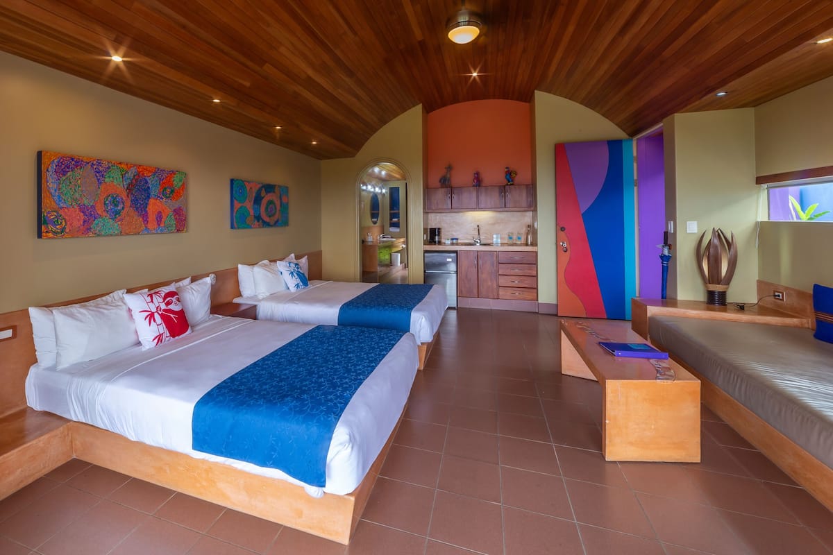 A hotel room with two beds, a small kitchenette, and a bathroom.