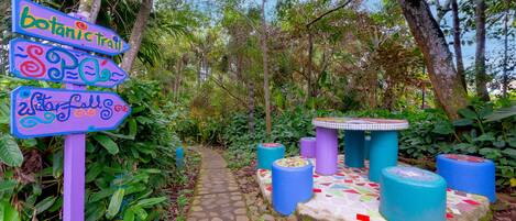 A garden pathway with directional signs, a mosaic-tiled table, and colorful cylindrical stools.