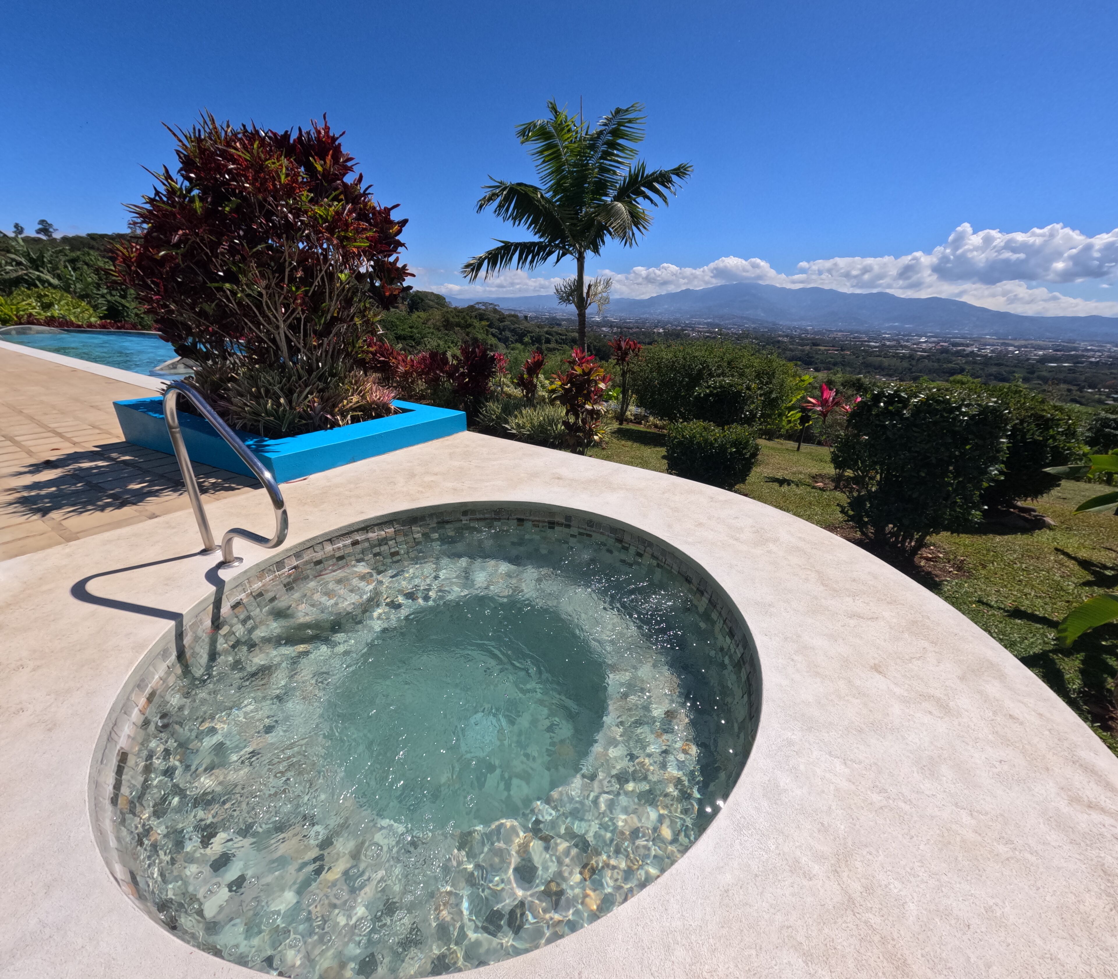 A hot tub with a clear view of mountains and a pool in the background.