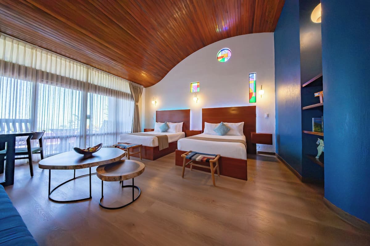 A hotel room with two beds, a dining table, and a small seating area.