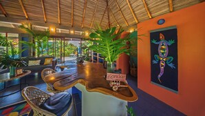 A bar area with a wooden counter, wicker chairs, and a large plant. - Xandari Resort And Spa (San Isidro)