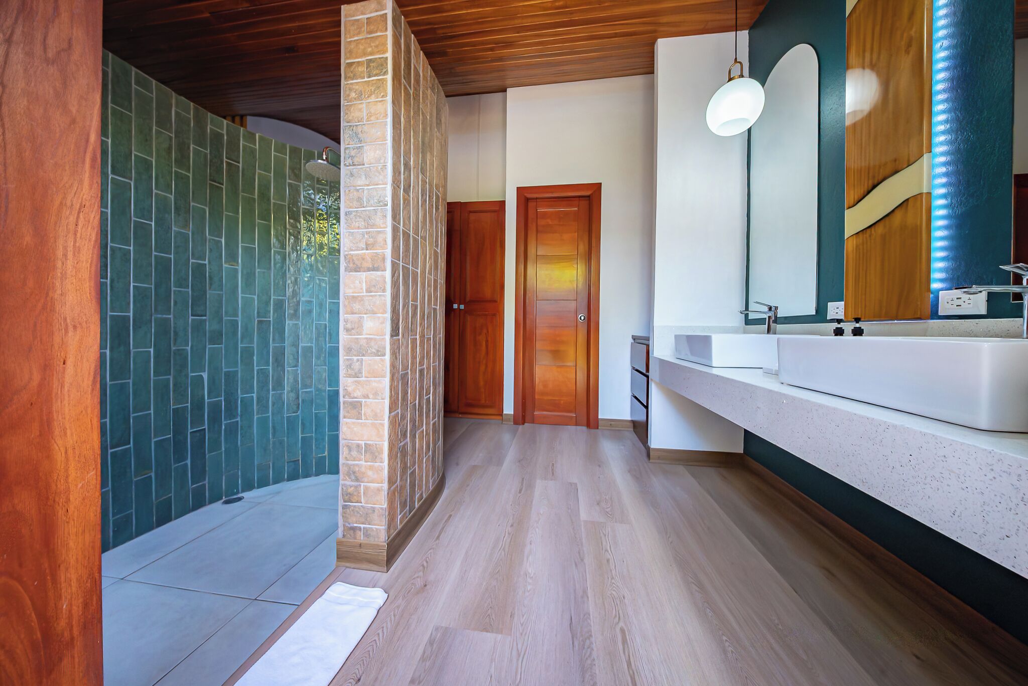 A modern bathroom with a stone wall, wooden door, and a large mirror.