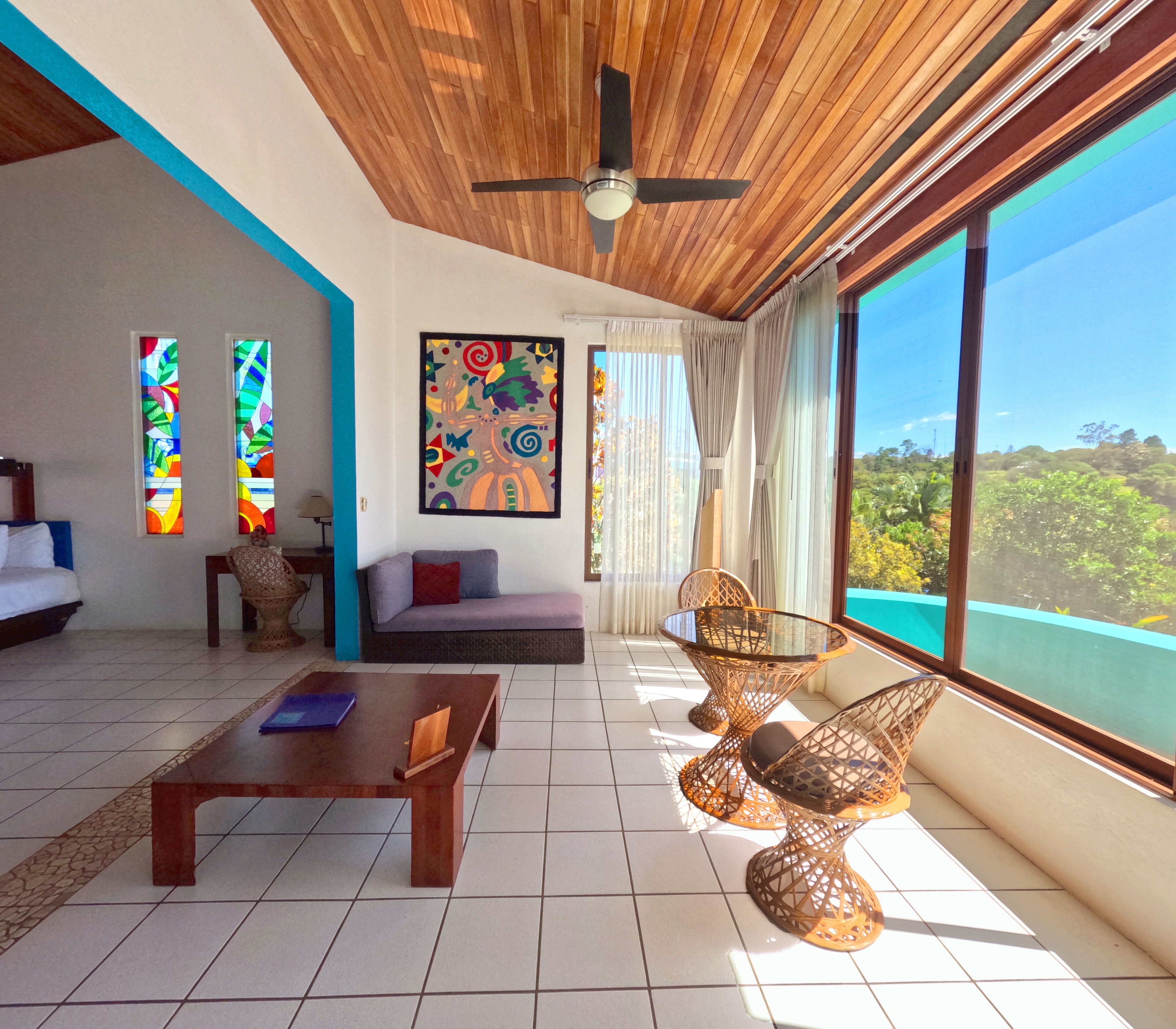 Uma sala de estar espaçosa com teto de madeira, janelas amplas, ventilador de teto e vista para o exterior.