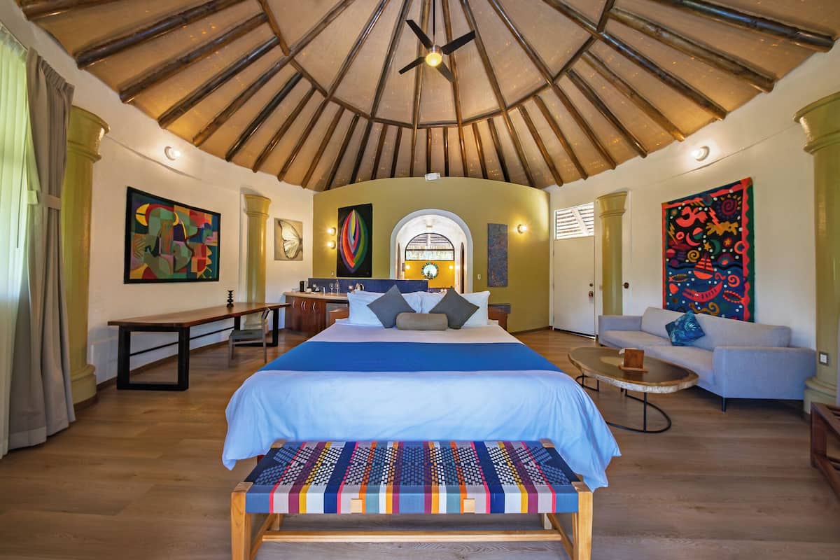 A spacious room with a large bed, a bench, a sofa, and a dining area.