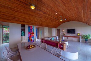 A modern kitchen with a wooden ceiling, a dining area with white chairs, and a TV mounted on the wall. - Xandari Resort And Spa (San Isidro)