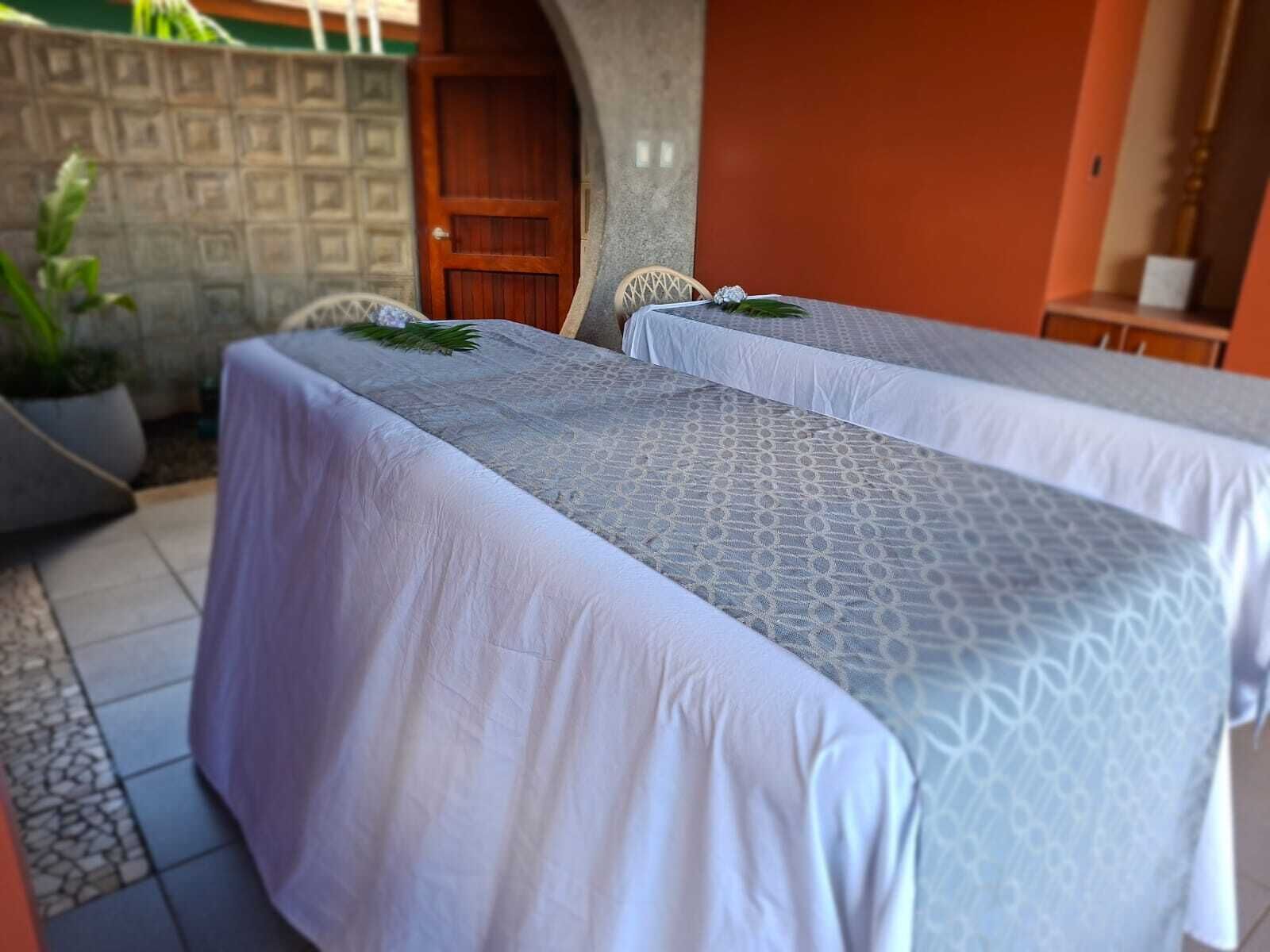 A room with two beds covered in white linens, a wooden door, and a small table with a chair.