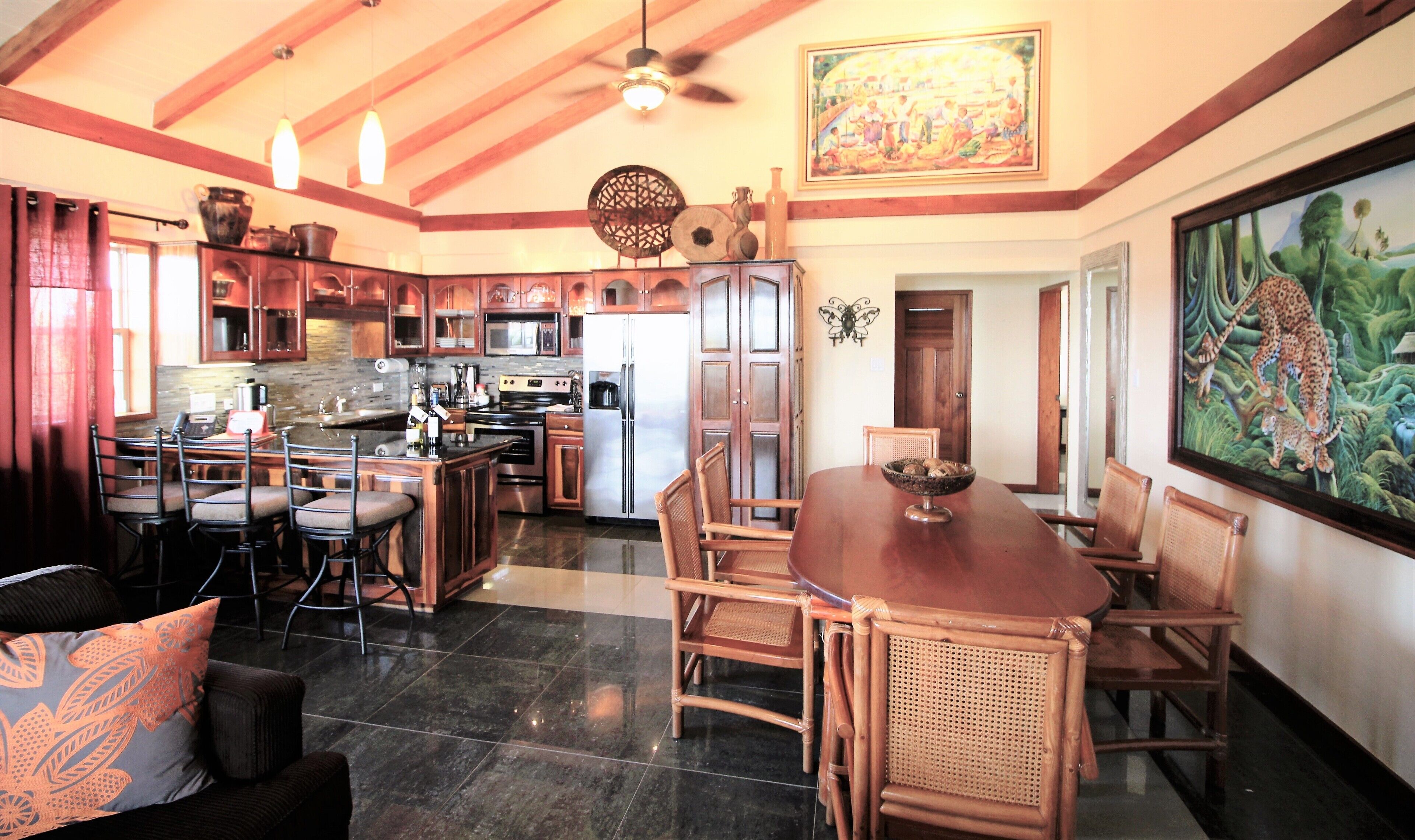 A spacious kitchen with modern appliances, a dining area with wooden furniture, and a large painting on the wall.