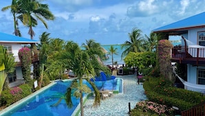 A resort pool area with a stone pathway, palm trees, and a view of the sea. - Chabil Mar Luxury Villas - Guest Exclusive Beach Resort (Placencia)