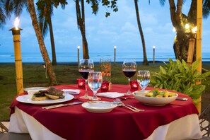 Une table dressée pour un repas, avec vue sur l’océan, entourée de palmiers.