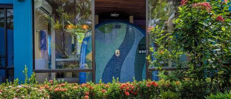 A building with a blue exterior, large glass windows, and a mosaic design on the wall.