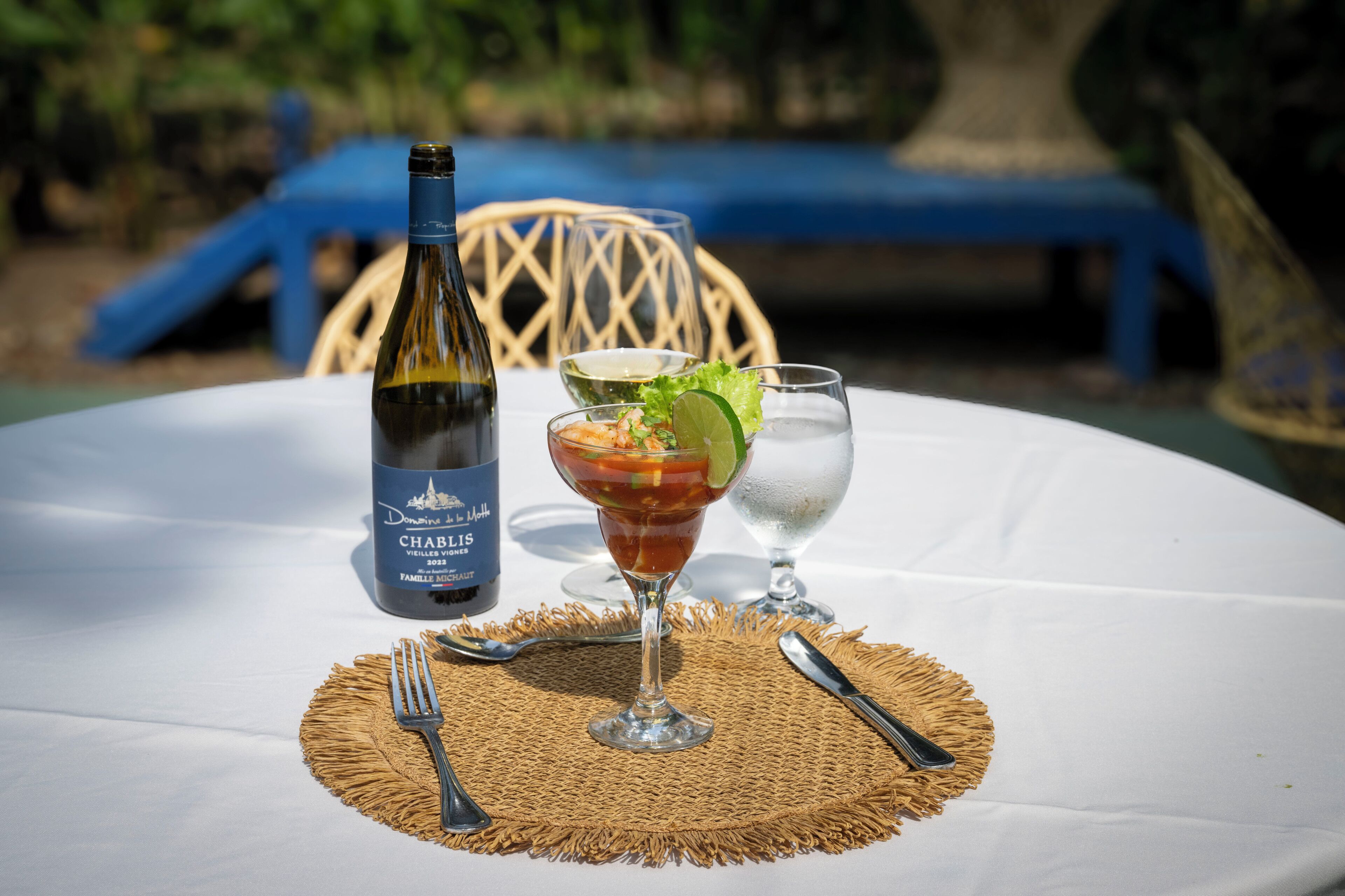 A table with a bottle of wine, a cocktail glass, and a water glass on a white tablecloth.