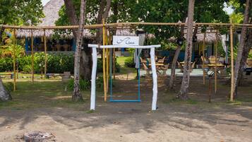 A beachside area with a swing set, a sign reading "Cima," and thatched-roof structures in the background.
