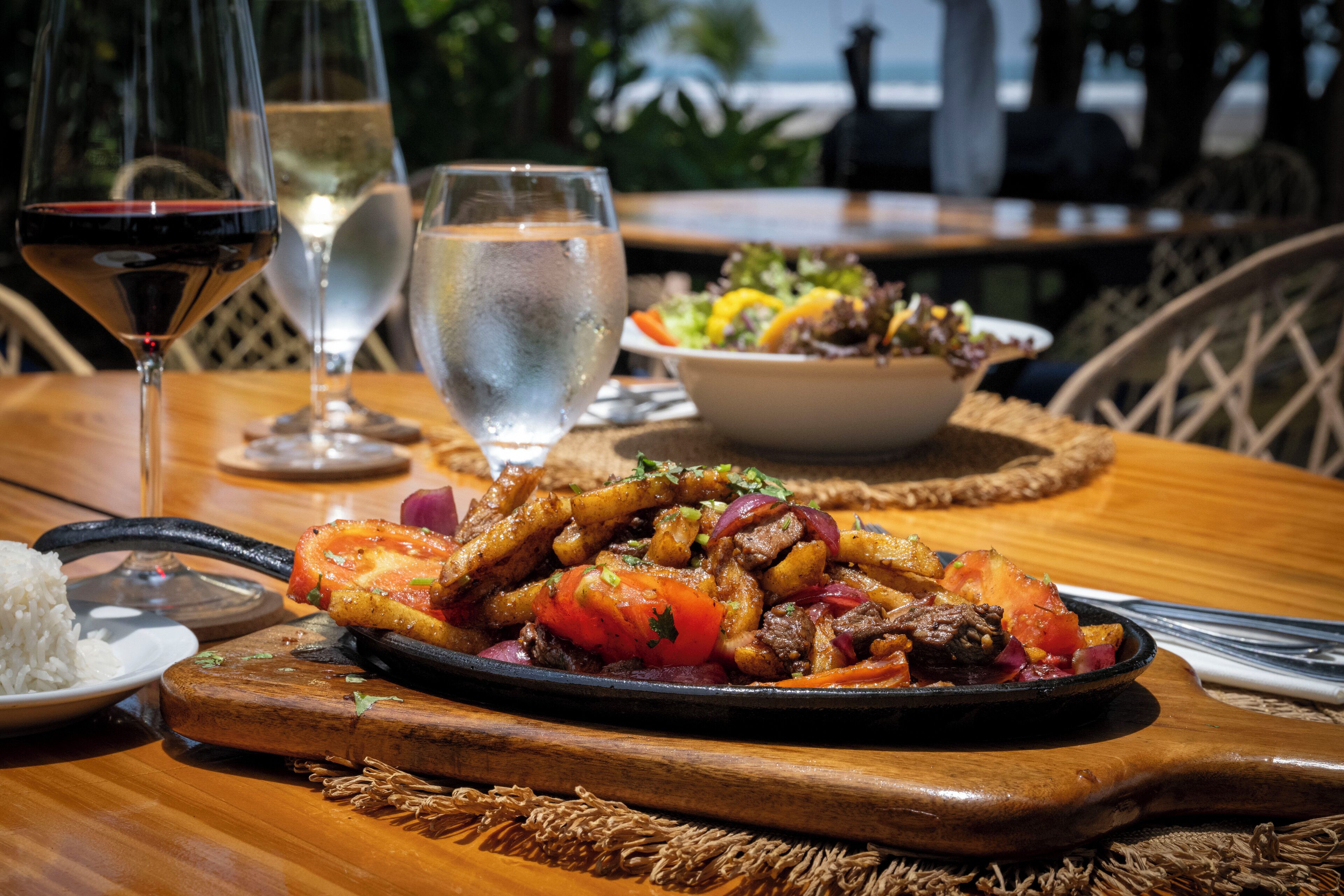 A wooden table with a meal, a glass of red wine, and a glass of water.