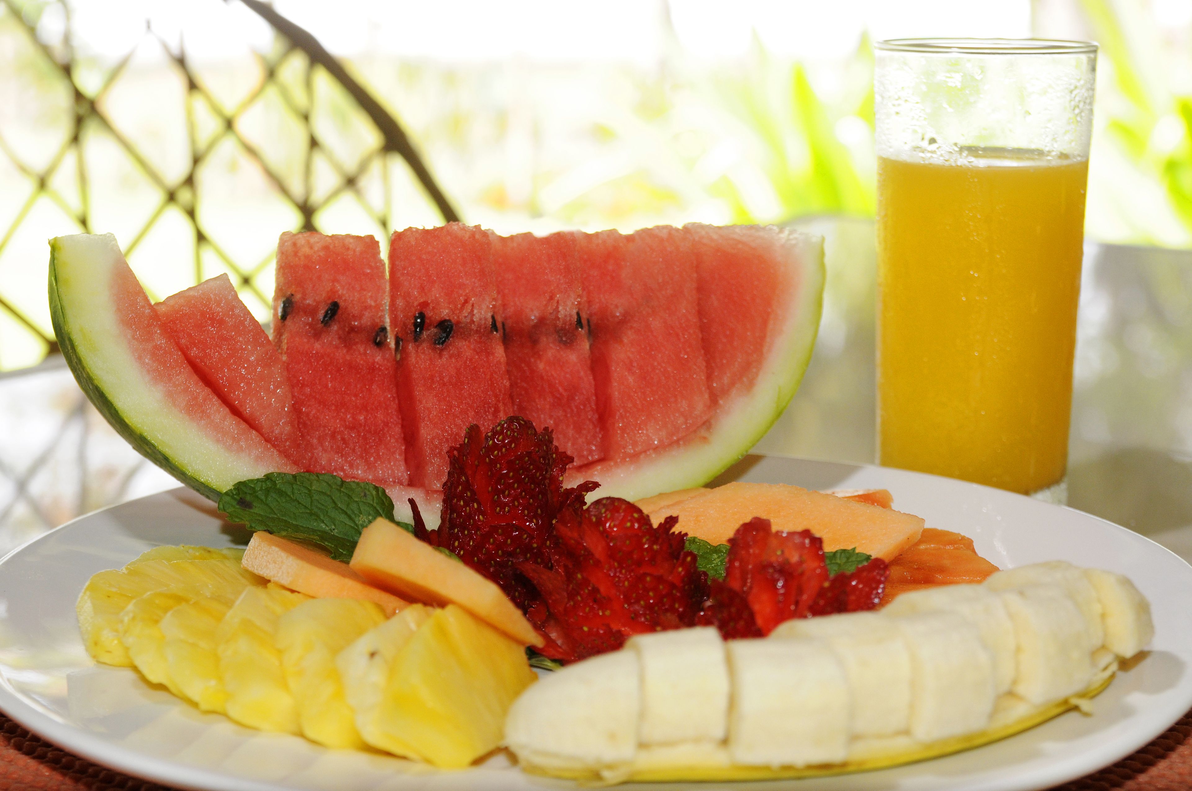 A plate of sliced fruits and a glass of orange juice.