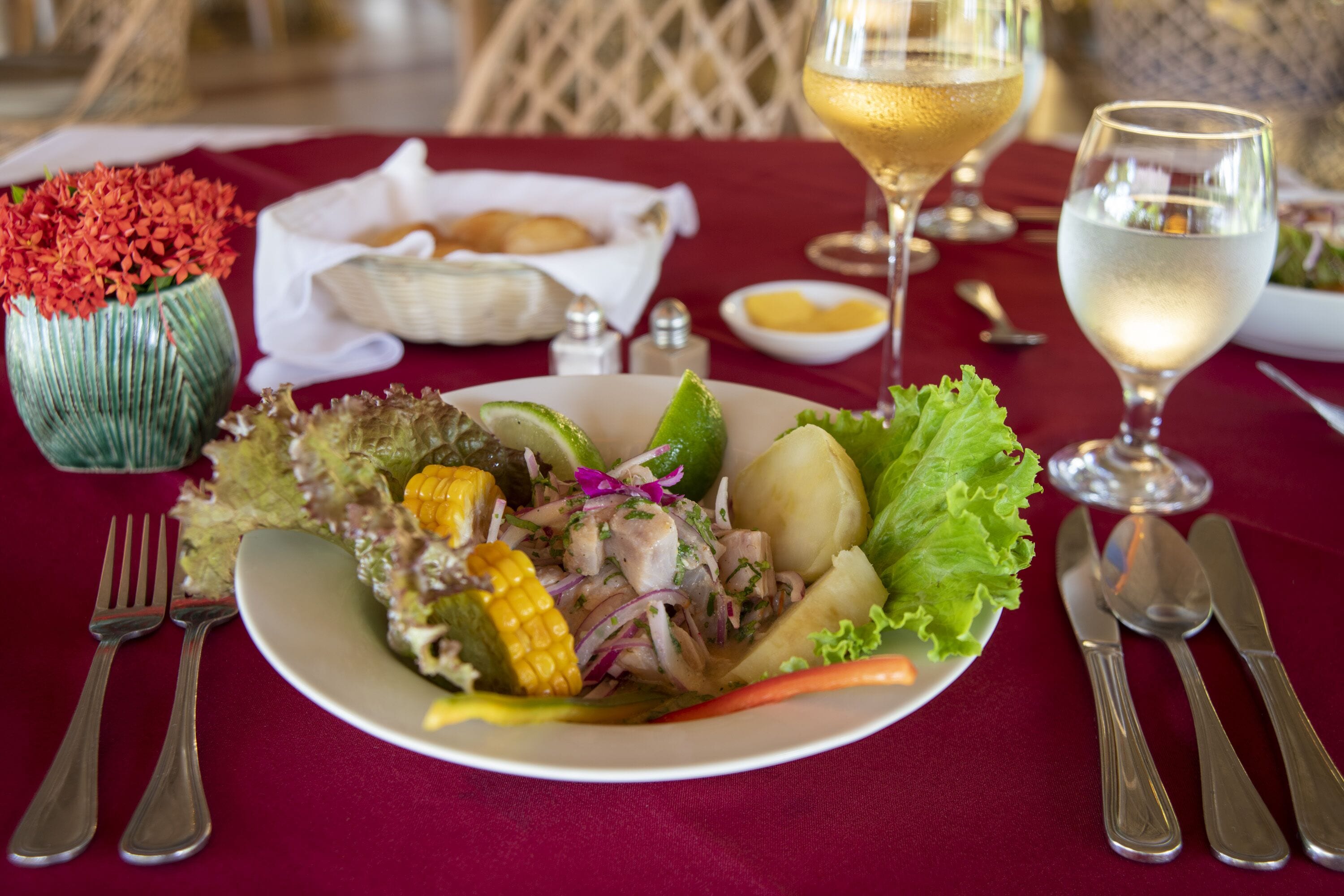 A dining table with a plate of salad, a glass of wine, and silverware.