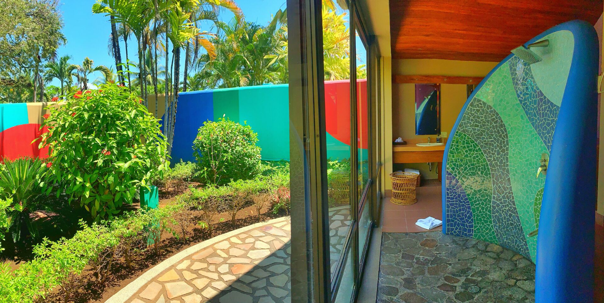 Un jardín tropical con un sendero de piedra que lleva a un baño con un muro de mosaicos.