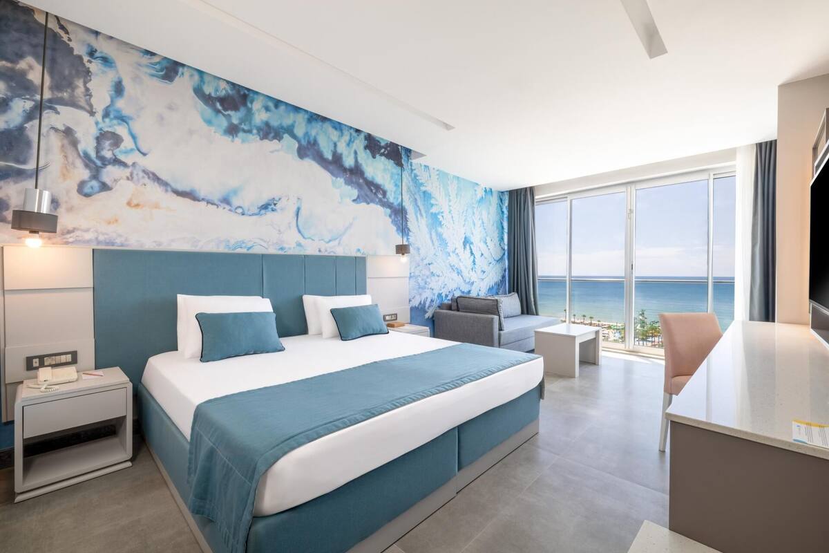 Una habitación de hotel moderna con una cama grande, un escritorio, una silla y vistas al mar.