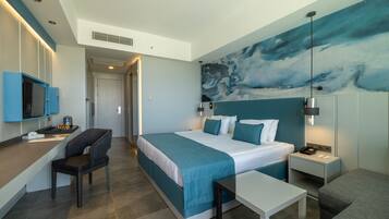 A modern hotel room with a large bed, a desk with a chair, a small table, and a nightstand with a lamp.