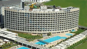 Un hotel grande de varios pisos con un patio central, múltiples piscinas y una zona en la azotea con un tobogán de agua.