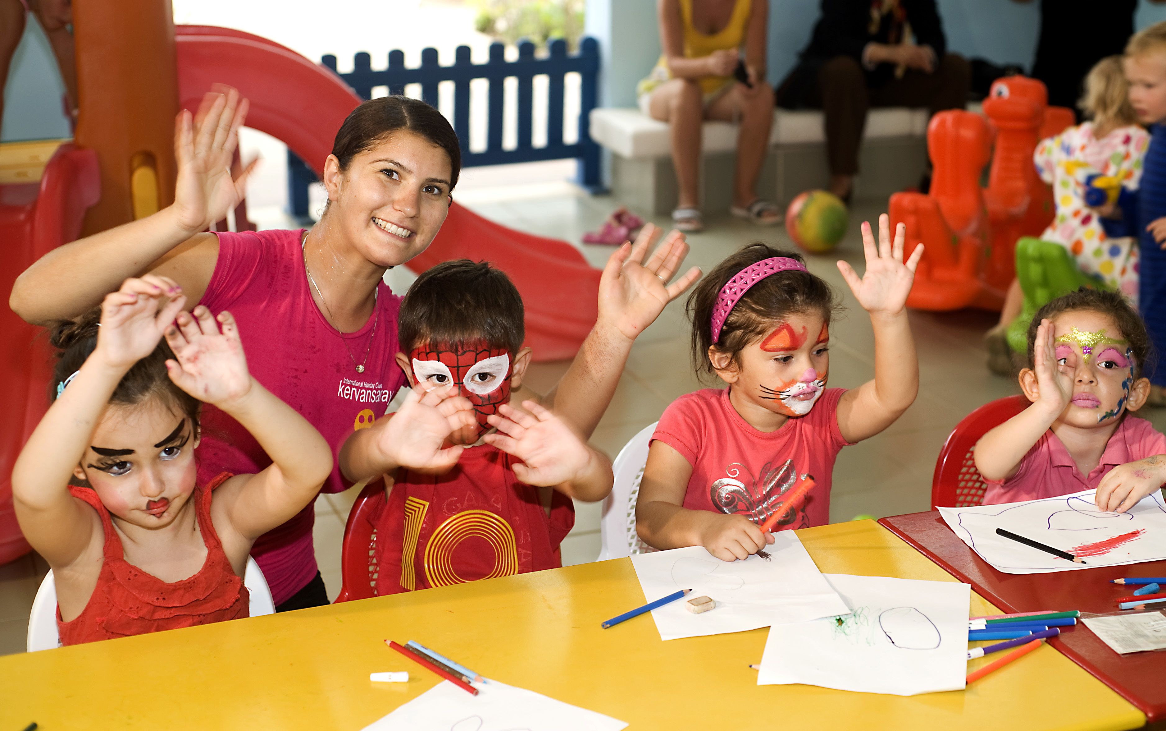 A group of children engaged in a face painting activity at a table with art supplies.