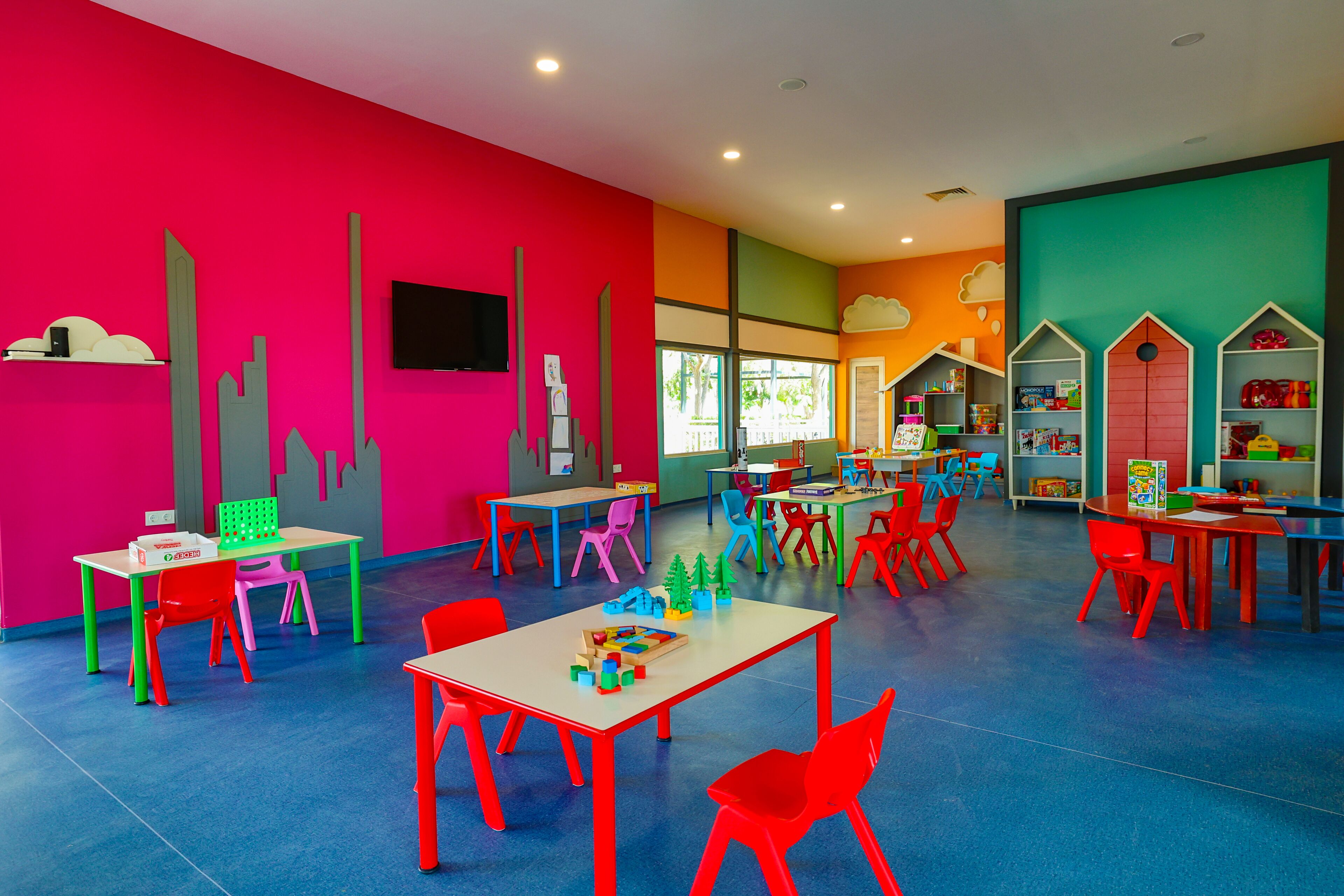 A brightly colored children's playroom with tables, chairs, and educational toys.