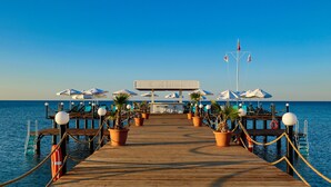 Un muelle de madera que lleva a una zona de playa con sombrillas y plantas en macetas.