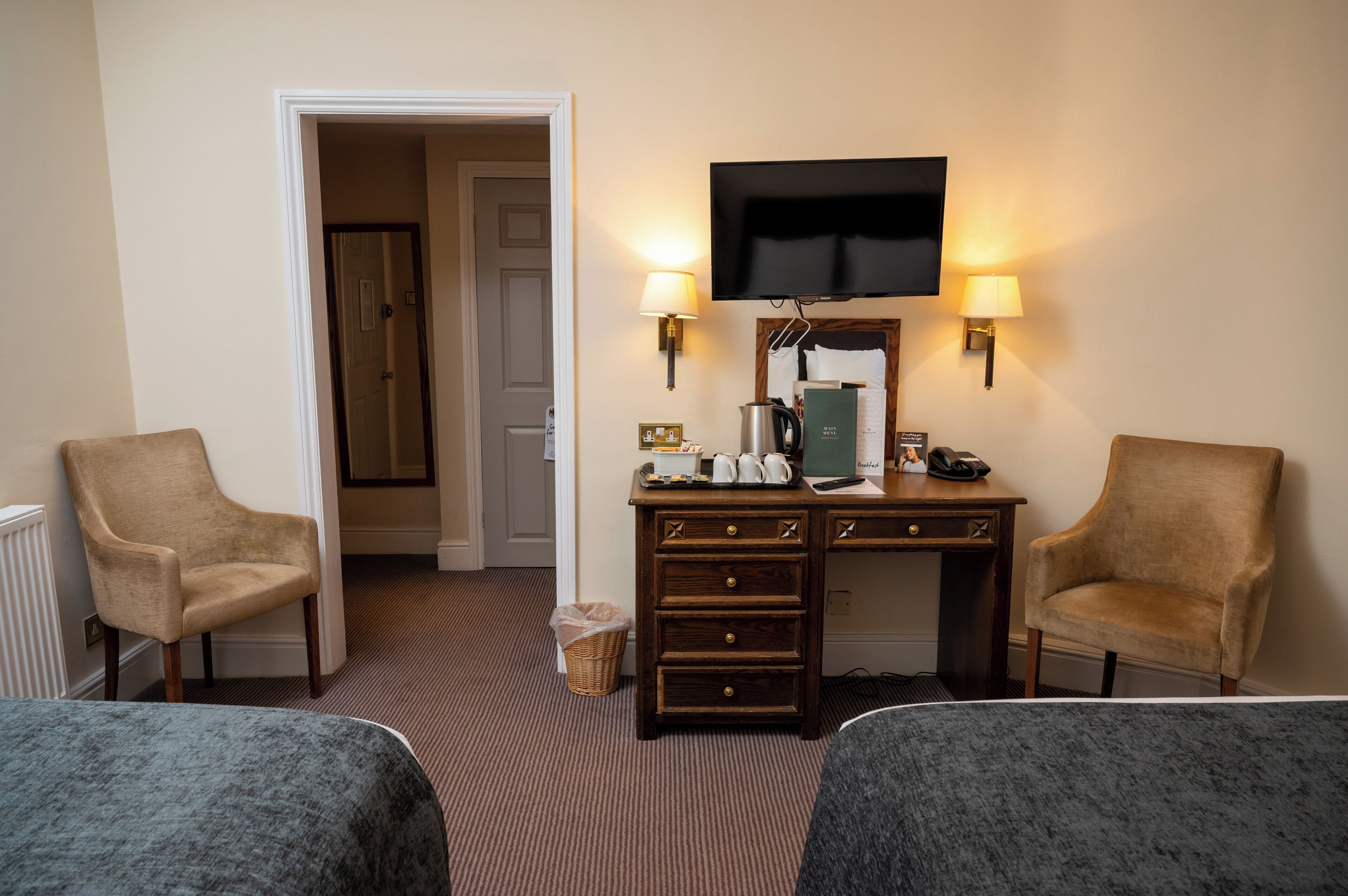 Habitación de hotel con dos camas, un escritorio, un televisor de pantalla plana, dos lámparas y un cesto de basura.