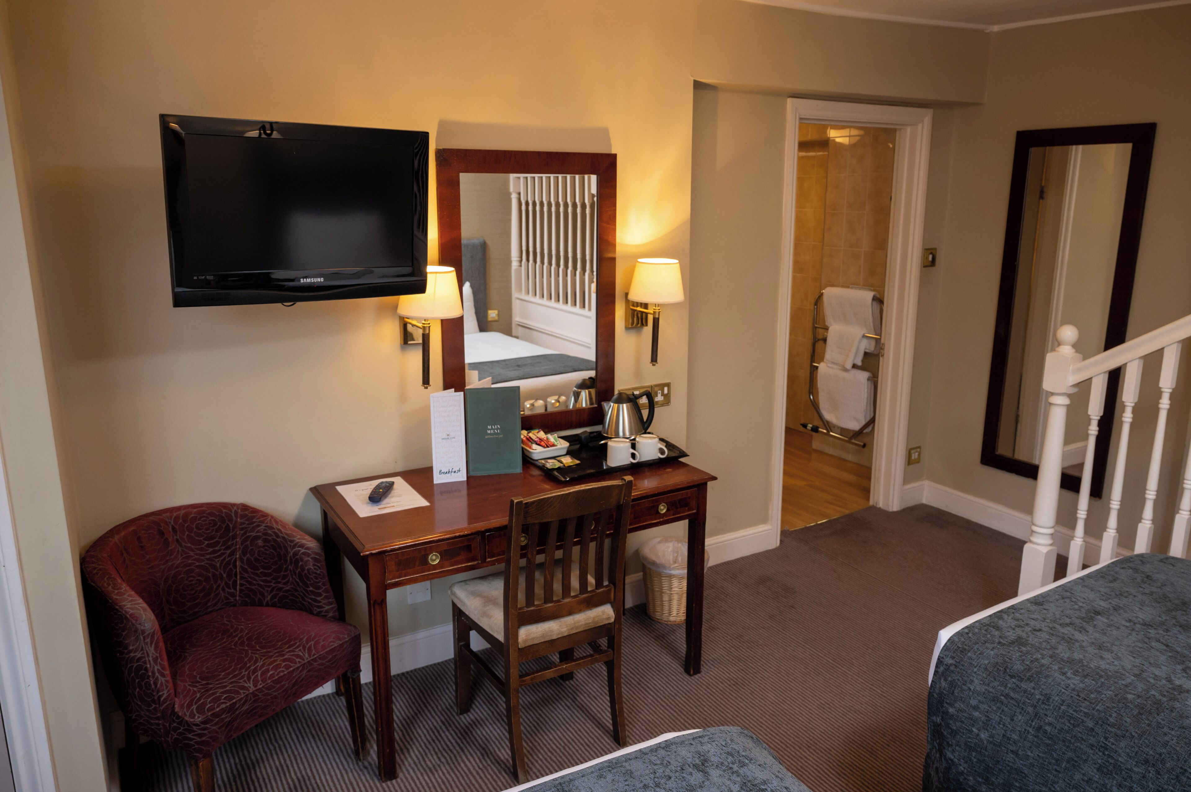 Habitación de hotel con televisor de pantalla plana, escritorio con silla, cama, baño con inodoro y ducha, y una escalera.