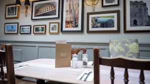 A dining table with a menu sign, salt and pepper shakers, and a chair with a floral cushion. - Castle And Ball by Greene King Inns (Marlborough)