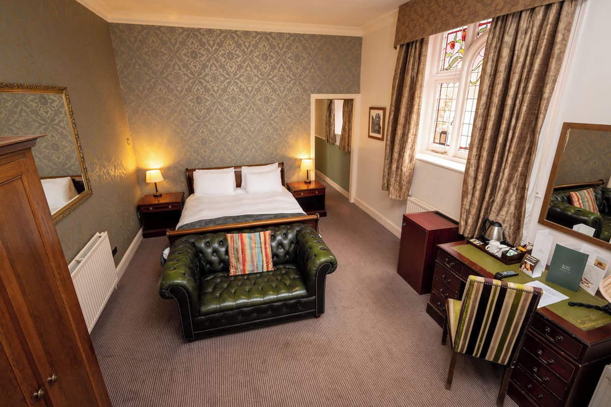 A hotel room with a large bed, a leather sofa, a desk with a telephone, and a window with curtains.