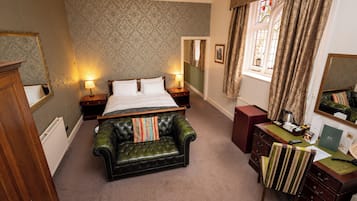 Quarto de hotel com cama grande, sofá de couro, escrivaninha com telefone e janela com cortinas.