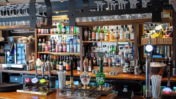 A bar area with multiple taps, shelves of bottles, and glasses on display. - Castle And Ball by Greene King Inns (Marlborough)