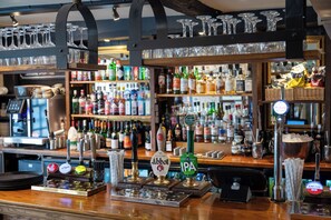 A bar area with multiple taps, shelves of bottles, and glasses on display. - Castle And Ball by Greene King Inns (Marlborough)