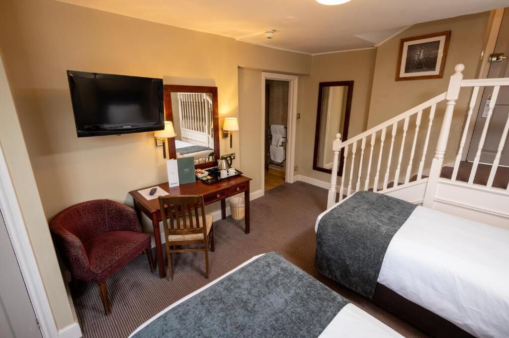 A hotel room with a bed, a desk with a chair, a television, and a staircase.