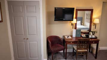 Een hotelkamer met een grote witte deur, een flatscreen televisie aan de muur, een bureau met een stoel, een bed met hoofdeinde en twee wandlampen.